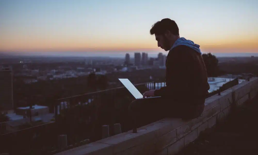 man sitting on concrete brick with opened laptop on his lap