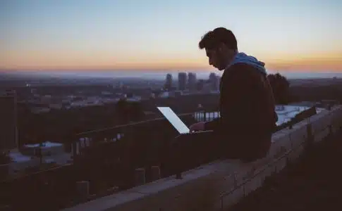 man sitting on concrete brick with opened laptop on his lap